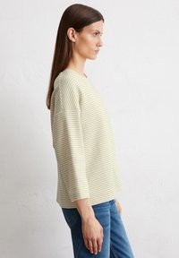 Haut rayé de couleur crème avec des manches 3/4 et une coupe décontractée. Fabriqué en tissu doux, il présente des rayures horizontales marron.