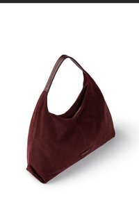 Burgundy suede shoulder bag with a smooth texture, curved shape, and a single handle; features a zippered opening and a gold-accented logo.