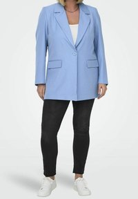 Blazer azul claro con solapas en pico, cierre de un botón y bolsillos frontales, combinado con jeans skinny negros y zapatillas blancas.