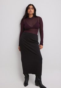 Burgundia pikkade varrukatega sobiv topp, millel on soonikkoes, on kihtidena musta keskmise pikkusega seeliku peal. Modell kannab musti põlvini ulatuvaid saapaid.