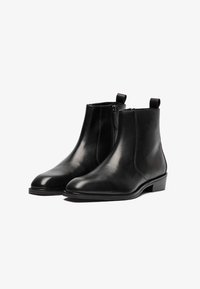 Botas de cuero negro hasta el tobillo con textura suave, puntera redonda, cierre lateral con cremallera y tira en la parte posterior. Tacón bajo apilado.