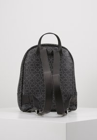 Czarny plecak z teksturowaną, wzorzystą powierzchnią z powtarzającym się logo. Wyposażony w regulowane skórzane paski i górny uchwyt.