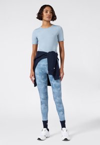 Jasnoniebieska dopasowana bluzka z krótkim rękawem, w połączeniu z szortami w niebieski wzór moro średniego wzrostu. Granatowy sweatshirt związany w talii, białe buty sportowe.