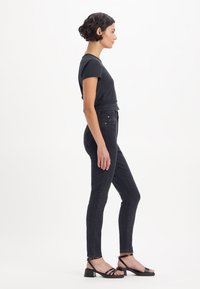 Svart tettsittende t-skjorte med korte ermer, kombinert med mørke smale jeans. Svart sandaler med stropper har en tykk hæl og justerbar stropp.