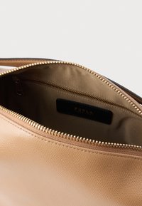 Beige læderpose med gyldent lynlås, foret med glat stof indvendigt; sort etiket med "FURLA"-logo synligt indeni.