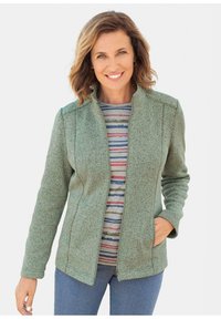 Groene fleecestyle jas met een rits aan de voorkant, hoge kraag en zijzakken, gedragen over een gestreept shirt, gecombineerd met blauwe jeans.