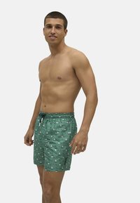 Bañador verde con un patrón de velero, cinturilla elástica y cordón. El material parece ligero y tiene una textura suave.
