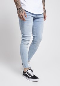Vaqueros ajustados de un azul claro, hechos de denim, con una textura suave y un desvanecimiento mínimo, combinados con zapatillas en blanco y negro.