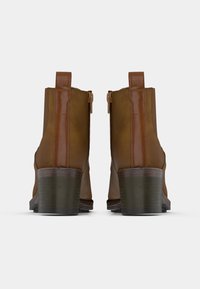 Brown leather ankle boots with a smooth finish, featuring a block heel and a side zipper. The design includes reinforced stitching and pull tabs.