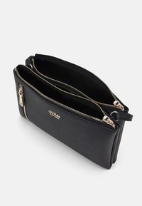 Schwarze Lederhandtasche mit Textur, zwei Reißverschlussfächern, goldfarbenen Hardware-Details und schlankem Design für einfaches Tragen.