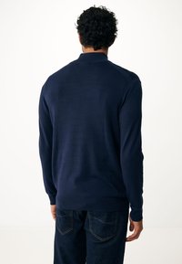 Marineblauwe gebreide trui met een kraag, lange mouwen en een textured oppervlak, gecombineerd met donkere spijkerbroek.