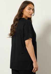 Zwarte, korte mouwen t-shirt met een losse pasvorm. Het heeft een ronde halslijn en een klein grafisch ontwerp op de voorkant. Soepele textuur.