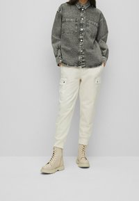 Chemise en denim gris à boutons avec deux poches poitrine, associée à un pantalon de jogging écru et des bottines beiges à lacets. Texture lisse.