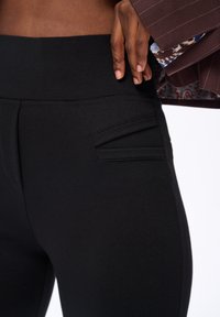 Czarne legginsy o gładkiej fakturze, z małą kieszonką po boku i wysokim pasem dla idealnego dopasowania. Prosty design i wszechstronny styl.