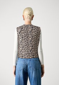 Leoparda raksta veste ar gludu tekstūru, ar noapaļotu kakla izgriezumu un bez piedurknēm, kombinēta ar ziliem augstās jostasvietas džinsiem.