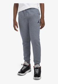 Pantalones de chándal grises con una cinturilla elástica y puños acanalados, que cuentan con un logo Jumpman en negro. Combinados con zapatillas deportivas negras y blancas.