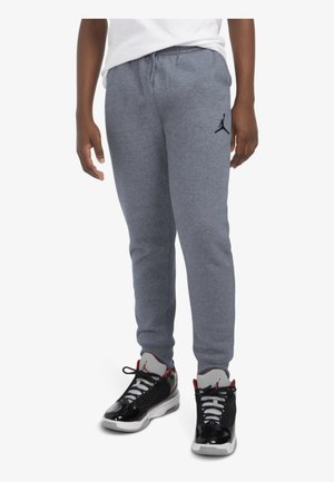 Pantalones de chándal grises con una cinturilla elástica y puños acanalados, que cuentan con un logo Jumpman en negro. Combinados con zapatillas deportivas negras y blancas.