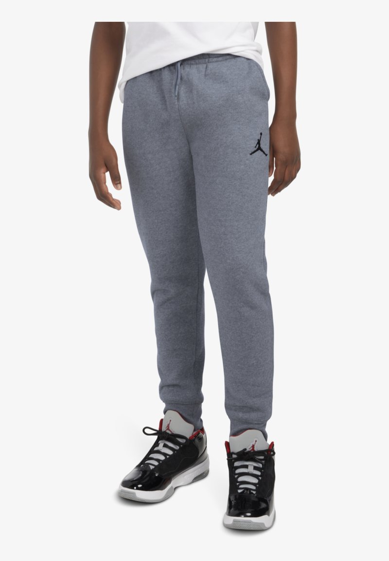 Pantalones de chándal grises con una cinturilla elástica y puños acanalados, que cuentan con un logo Jumpman en negro. Combinados con zapatillas deportivas negras y blancas.