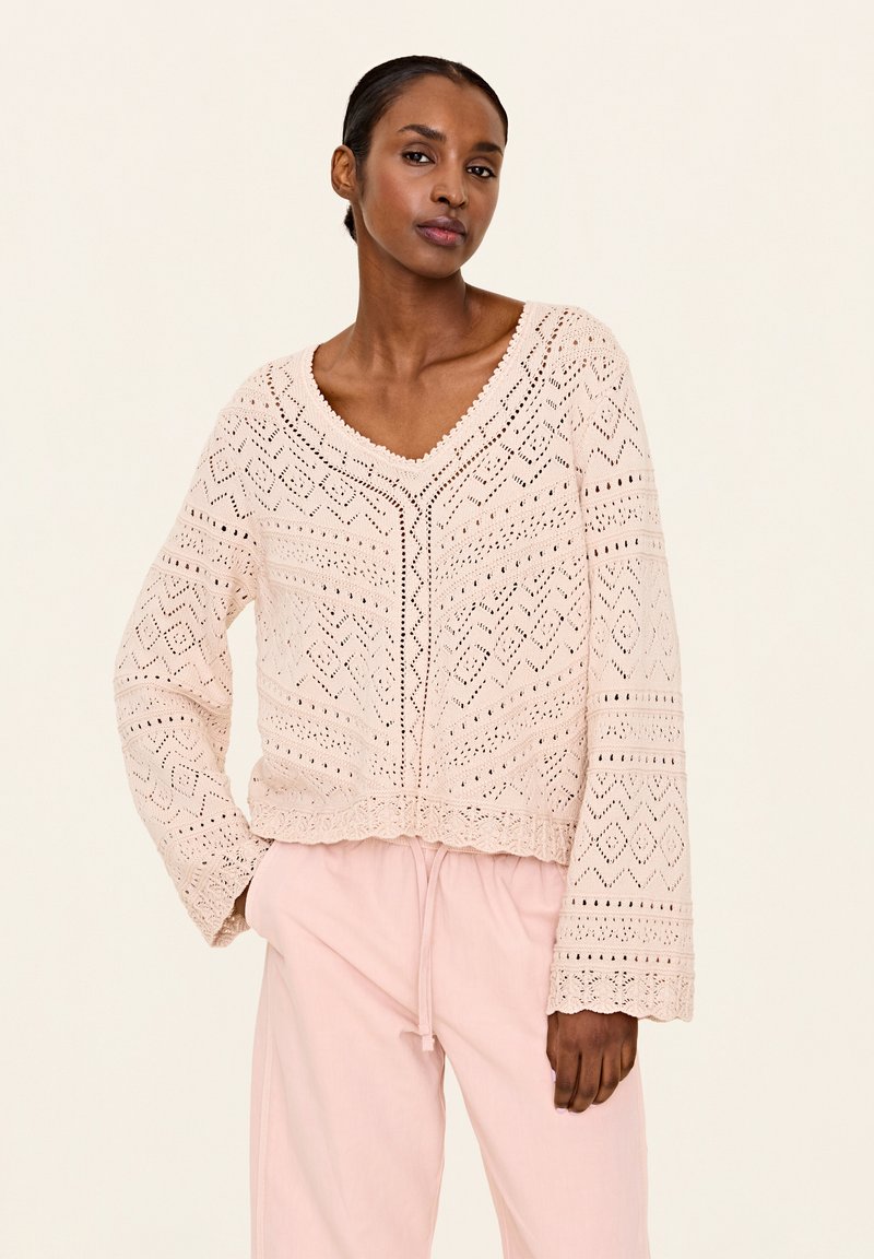 Helles rosa gestricktes Sweatshirt mit V-Ausschnitt, langen Ärmeln und komplizierten Rautenmuster- und Zickzackmustern. Verkürzter Stil mit gewelltem Saum.