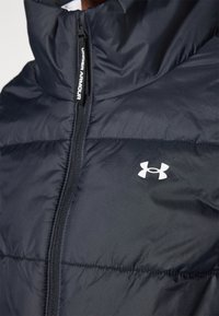 Marineblaue Daunenjacke mit hohem Kragen, ausgestattet mit einer Reißverschlussvorderseite und dem weißen Under Armour-Logo. Strukturierter, gestepptes Material.