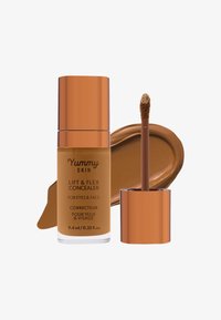 Yummy Skin Lift & Flex Concealer i en gjennomsiktig flaske har en varm brun nyanse med en blank kobberlokk og en doe-foot-applikator.