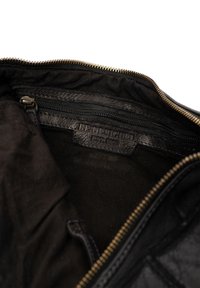 Interno in pelle nera di una borsa con zip, dotato di un'etichetta in pelle impressa "RE:DESIGNED EST. 2003" e una fodera in tessuto morbido.