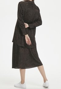 Långärmad mörkbrun klänning med leopardmönster, avslappnad passform, lagerdesign och sidöppning, tillsammans med vita sneakers.