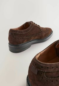 Chaussures en suède marron à lacets, dotées de détails en brogue, d'un bout arrondi et d'une semelle en caoutchouc noir avec un léger talon. Doublure intérieure lisse.