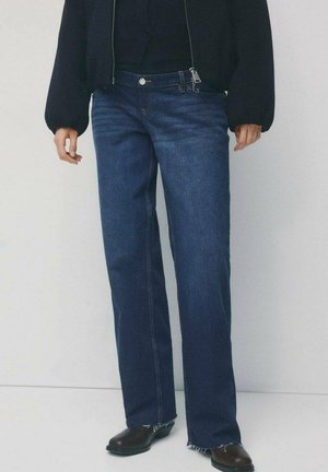 Proste jeansy w ciemnym niebieskim kolorze z pięcioma kieszeniami, postrzępionym dołem i kontrastującym żółtym przeszyciem, noszone z czarną krótką kurtką.