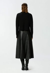 Crni skraćeni pulover, crna kožna suknja, crne čizme do koljena. Glatke teksture, uski kroj i elegantna silueta.