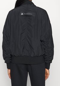 Black bomber jacket featuring a ribbed collar and cuffs, gathered detailing on sleeves, and a logo label on the back. Smooth fabric texture.