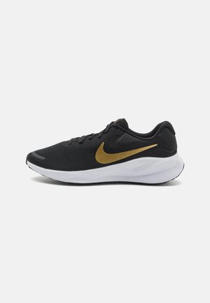 Zapatilla deportiva negra con logo dorado de Nike y suela blanca acolchada sobre fondo claro liso.