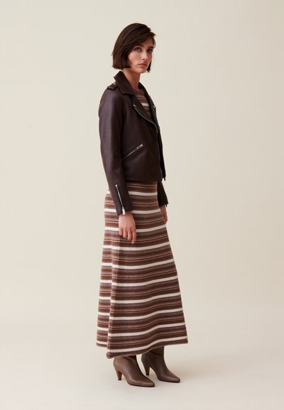Veste de motard en cuir marron avec des fermetures éclair argentées, associée à une jupe maxi en tricot rayée marron et crème, et des bottines à talons marron.
