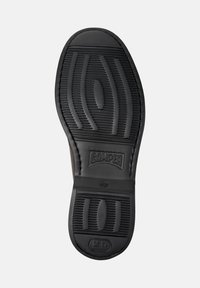 Suela de zapato de goma negra con patrones texturizados para agarre, con el nombre de la marca "CAMPER" estampado en el centro.
