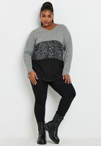 Grauer Strickpullover mit einem Mittelteil im Leopardenmuster, schwarzem Saum, kombiniert mit schwarzen Skinny-Jeans und schwarzen Ankle Boots.