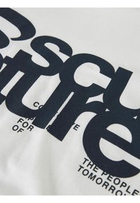 Camiseta de algodón blanca con gran texto negro y diseño abstracto. El texto está parcialmente oculto, con detalles en diferentes tamaños de fuente.