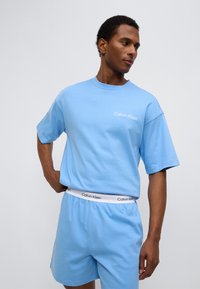 Γαλάζιο βαμβακερό t-shirt με κοντά μανίκια και μικρό λευκό λογότυπο. Συνδυάζεται με γαλάζια σορτς και λευκή ζώνη μέσης με λογότυπο.