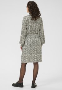 Rochie cu mâneci lungi, în dungi ondulate de culoare neagră și crem, cu un cordon la talie, tiv de lungime medie, asociată cu pantofi negri și ciorapi subțiri.