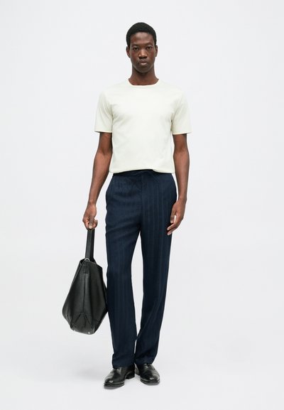 Hele halli lühikeste varrukatega särk, tumesinised triibulised püksid, must nahk-kott, mustad kingad. Lihtne disain ja lõdva istuvusega.