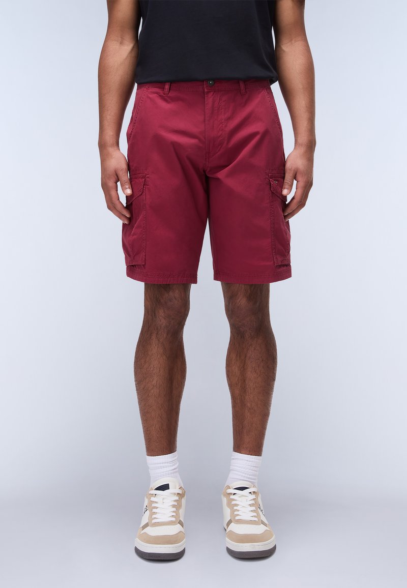 Pantaloni cargo bordeaux con due tasche laterali, realizzati in tessuto liscio. Abbinati a sneakers bianche e beige e calzini bianchi alla caviglia.