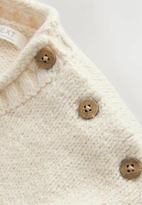 Pull tricoté couleur crème avec un motif texturé et des boutons en bois sur l'épaule pour la fermeture. Tissu doux et chaud.