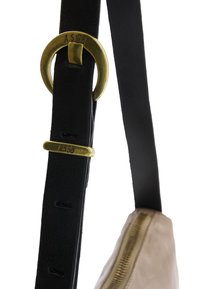 Sort læderrem med en messingring og accentstykke mærket "A.S. 98." Fastgjort til en beige taske med en metallynlås.