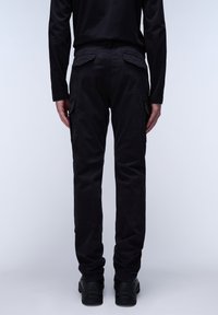 Czarne spodnie cargo mają wiele bocznych kieszeni, luźny krój i gładką fakturę. W zestawieniu z czarnymi butami, widok od tyłu.