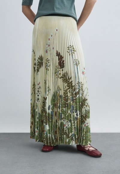 Falda maxi plisada en color crema claro, con un estampado floral con toques verdes y marrones. Combinada con zapatos planos marrón granate.