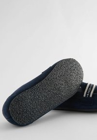 Scarpa slip-on in suede blu navy con suola in gomma testurizzata, accentuata da una fascia a righe e un dettaglio di branding sul lato, caratterizzata da una punta rotonda.