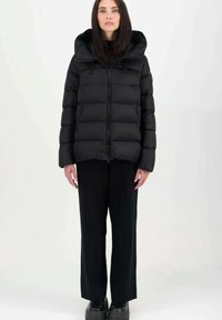 Giacca a vento nera con cappuccio, chiusura a zip frontale, design trapuntato e due fiocchi neri. Indossata con pantaloni neri a gamba larga e scarpe nere chunky.