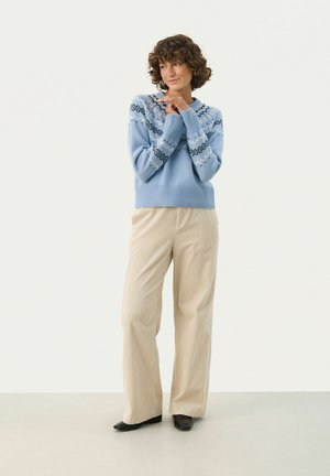 Light blue knitted sweater featuring a patterned yoke design in dark blue and white, paired with beige corduroy wide-leg pants and black shoes.