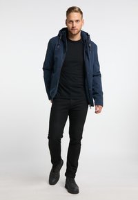 Giacca a vento blu navy con cappuccio e zip frontale, abbinata a una maglietta nera e jeans neri. Sneakers nere completano l'outfit.