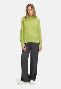 Pull en mailles vert vif avec un col haut et des manches amples, associé à un pantalon large gris foncé et des baskets blanches.