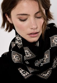 Sciarpa nera con intricati motivi geometrici in beige e bianco. Texture morbida con un design a anello, avvolta attorno al collo.